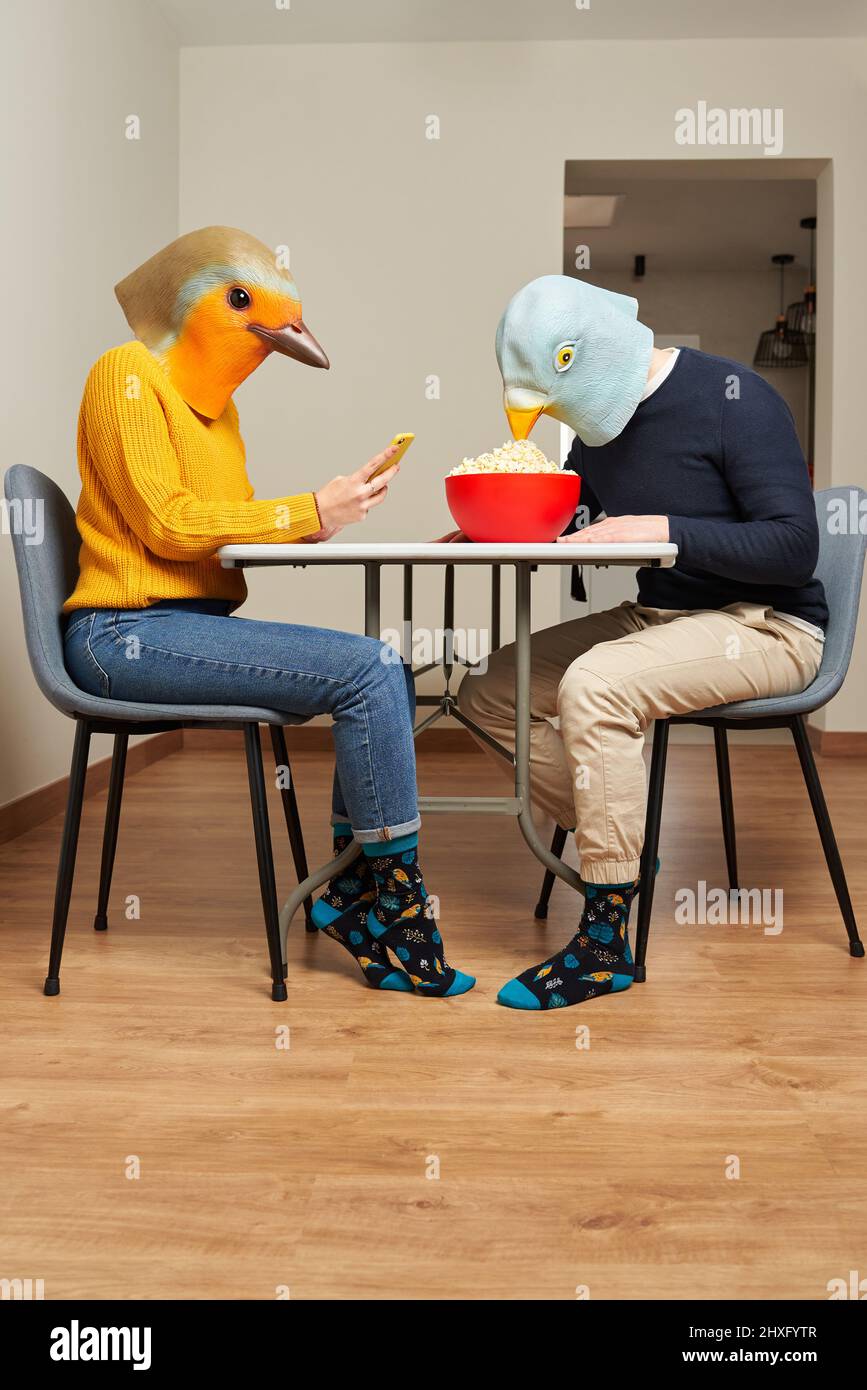 Ein Paar, das in Vogelmasken gekleidet ist, isst Popcorn am Tisch Stockfoto