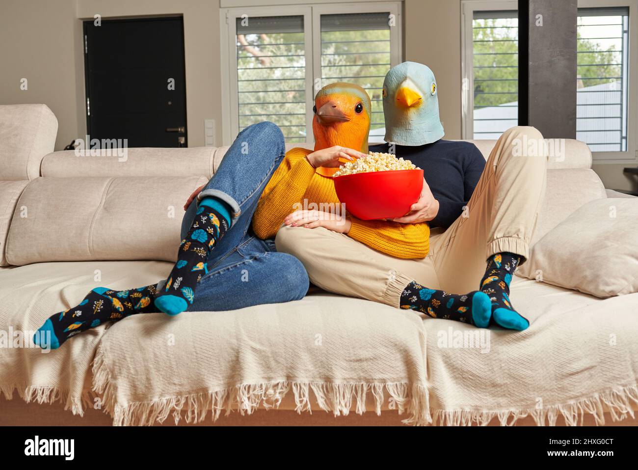Ein Paar mit Vogelmasken, das einen Film auf dem Sofa sieht Stockfoto