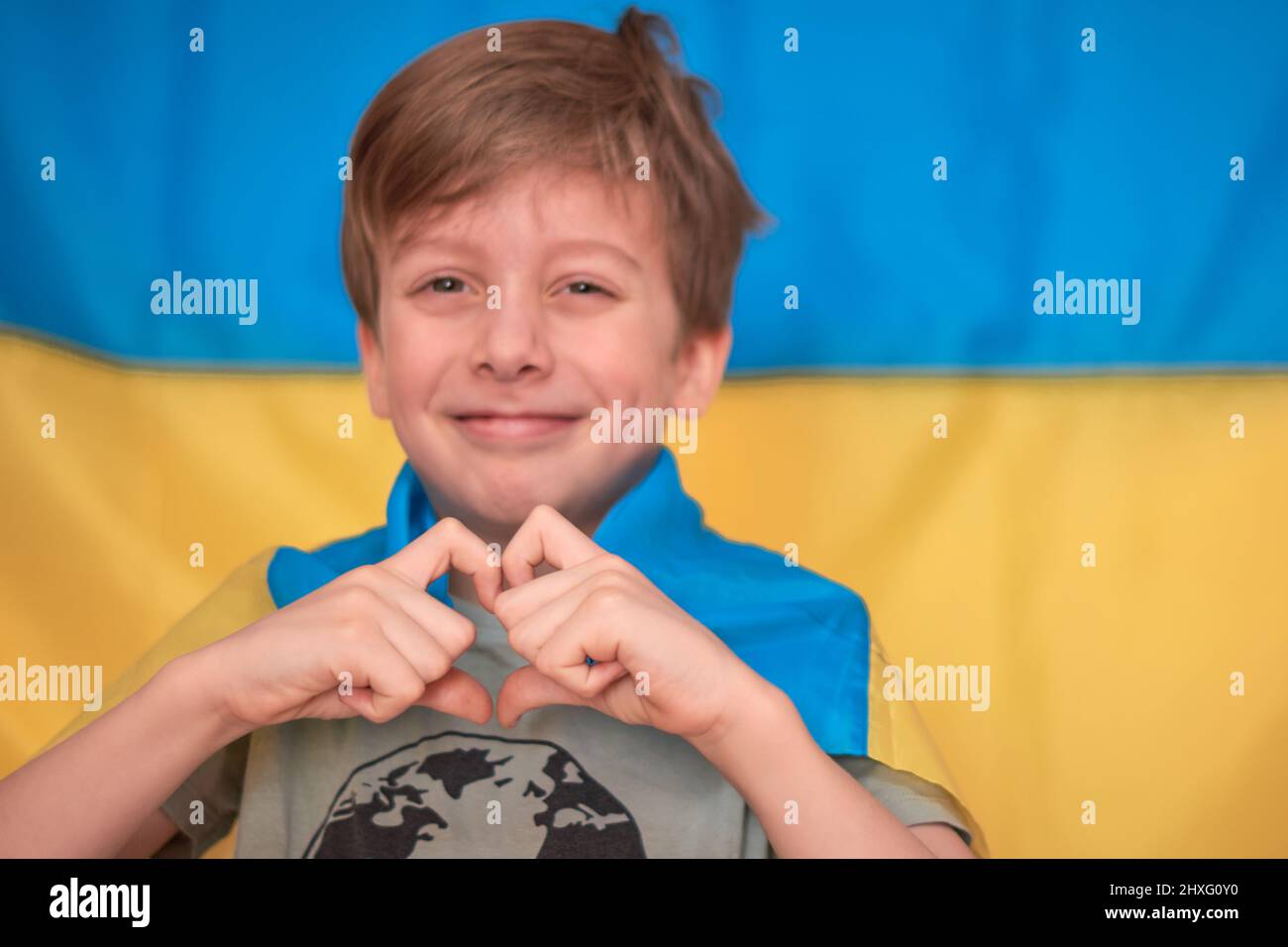 Junge hält ukrainische Flagge auf gelb-blauem Hintergrund in Händen. Die Kinder unterstützen die Ukraine mit Herzblut. Ukrainische Krise, russische Aggression in der Ukraine. Krieg Russlands gegen die Ukraine. Stockfoto