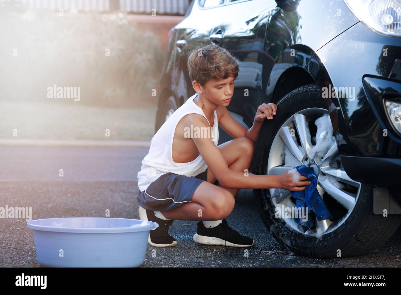 Scheuern Sie den ganzen Abrieb weg. Aufnahme eines jungen Jungen, der das Rad eines Autos wascht. Stockfoto