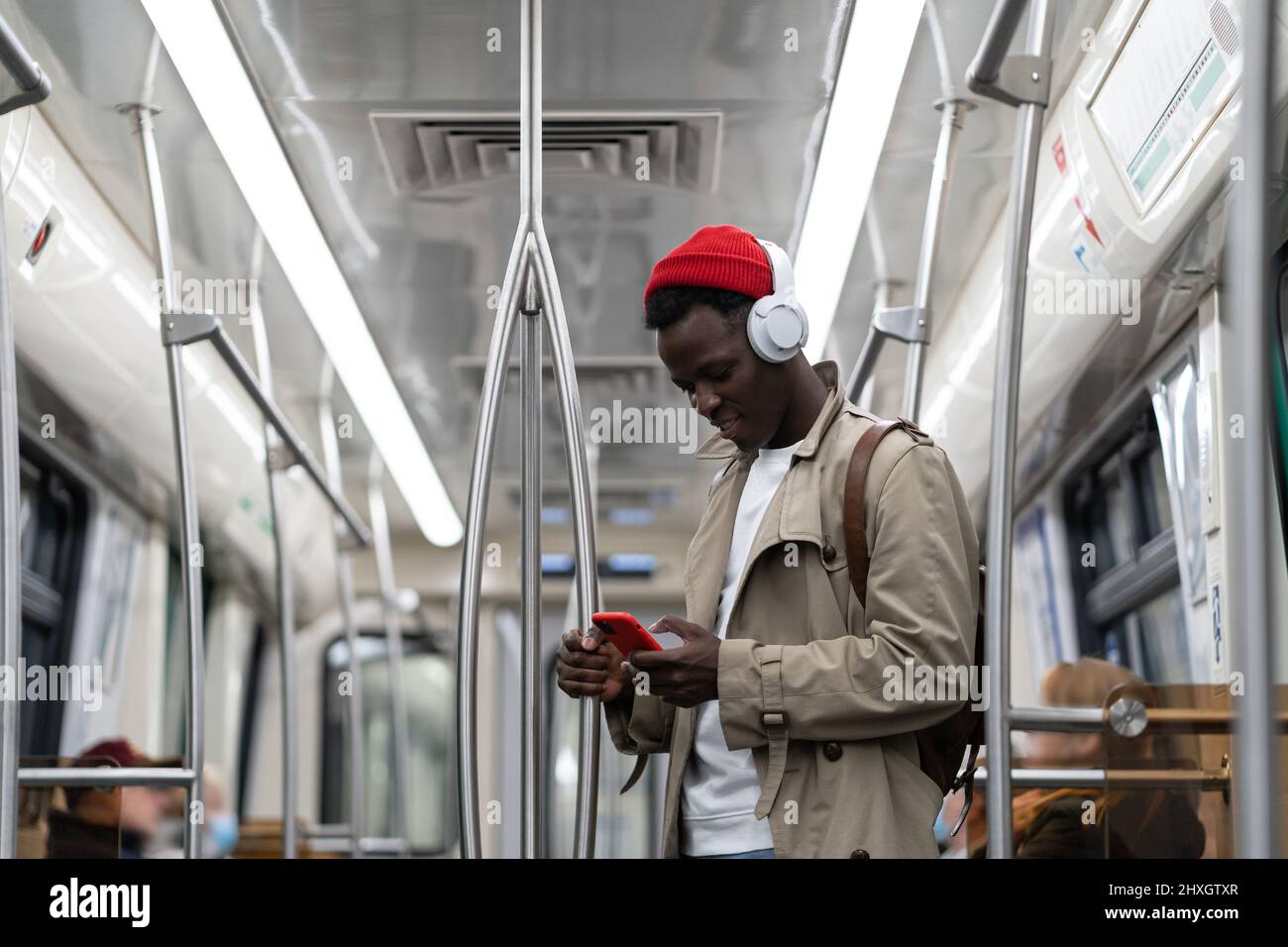 Schwarzer Hipster-Mann trägt kabellose Kopfhörer, hört die Musik, mit dem Smartphone in der U-Bahn Stockfoto