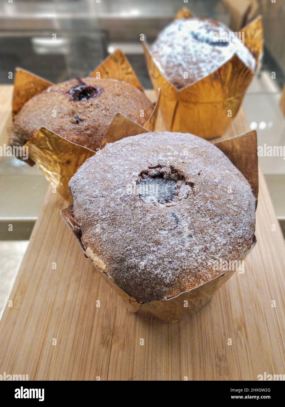 Schokoladen-Muffins mit Schokoladenfüllung in goldenem Papier auf Schaufenster eines Cafés, Cupcake-Konzept Stockfoto