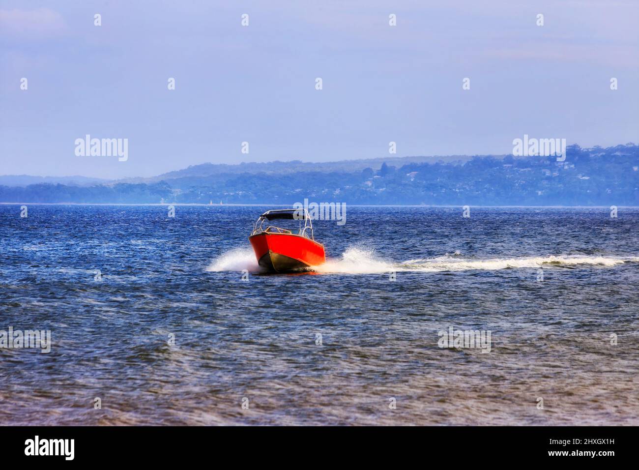 An einem sonnigen Sommertag steht ein kleines Motorboot auf der Oberfläche der Jervis Bay vor dem Callala Beach. Stockfoto