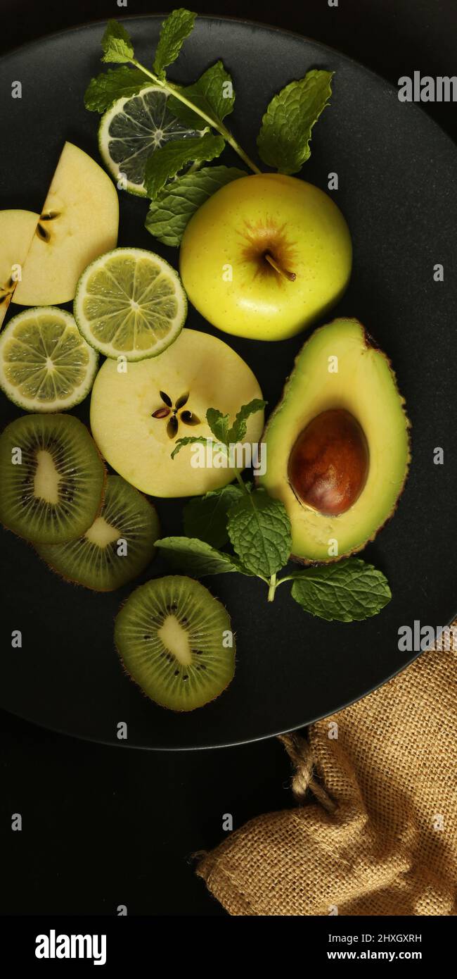 Fruchgelb Rand von verschiedenen Früchten, Draufsicht. Dramatisches Küchenkonzept von grünen Früchten auf schwarzem Hintergrund mit Leinwand. Flach liegend. Vertikaler Rahmen Stockfoto