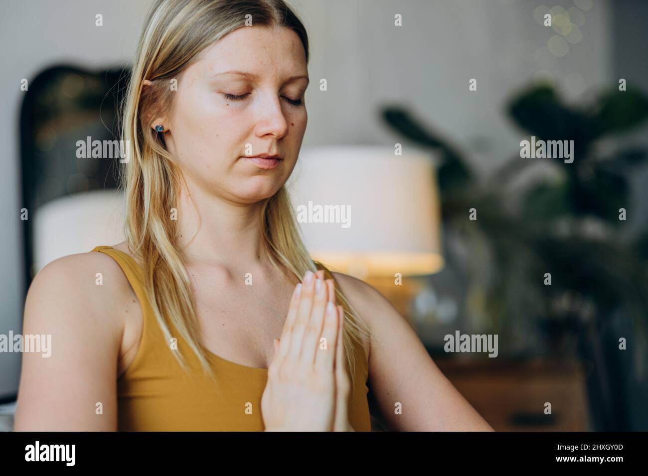 Eine athletische Frau mit blonden, lockeren Haaren und Tätowierungen in der Oberseite und Leggings meditiert mit einem breiten Lächeln in Lotushaltung auf der Yoga-Matte aus der Nähe Stockfoto