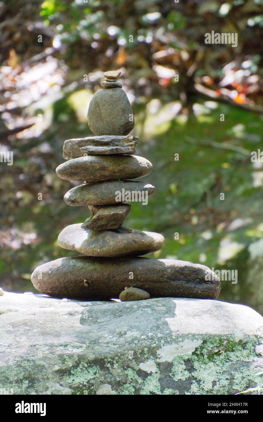 Ein Stapel von gestapelten Flusssteinen, die im Sommer einen fein balancierten Steinhaufen bilden, um einen Waldwanderweg zu markieren Stockfoto