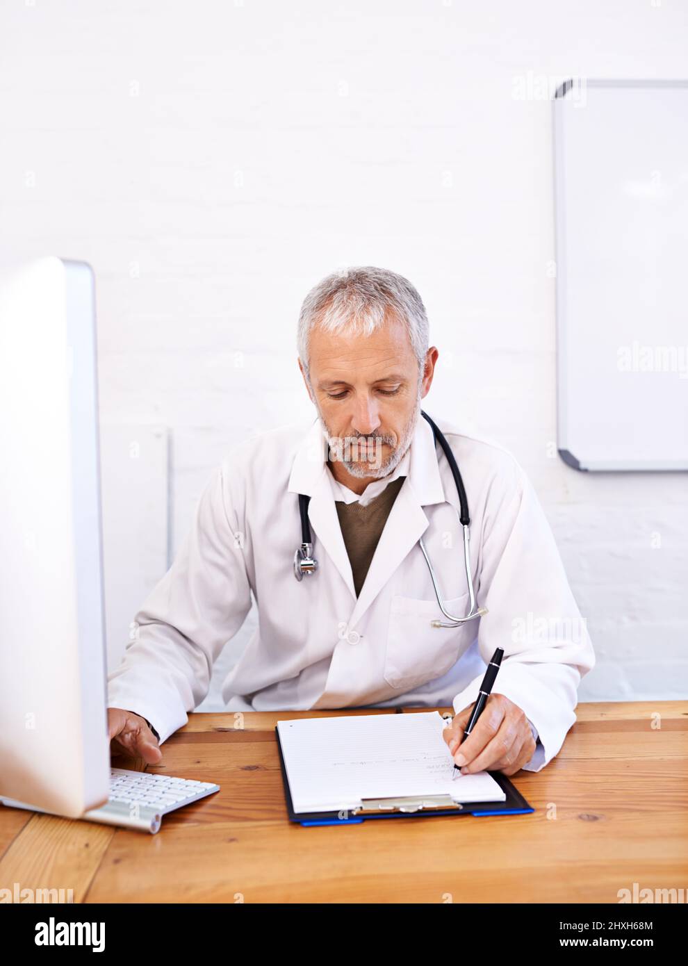 Online-Recherche zu Behandlungsoptionen. Aufnahme eines reifen männlichen Arztes, der an einem Desktop-Computer in seinem Büro arbeitet. Stockfoto