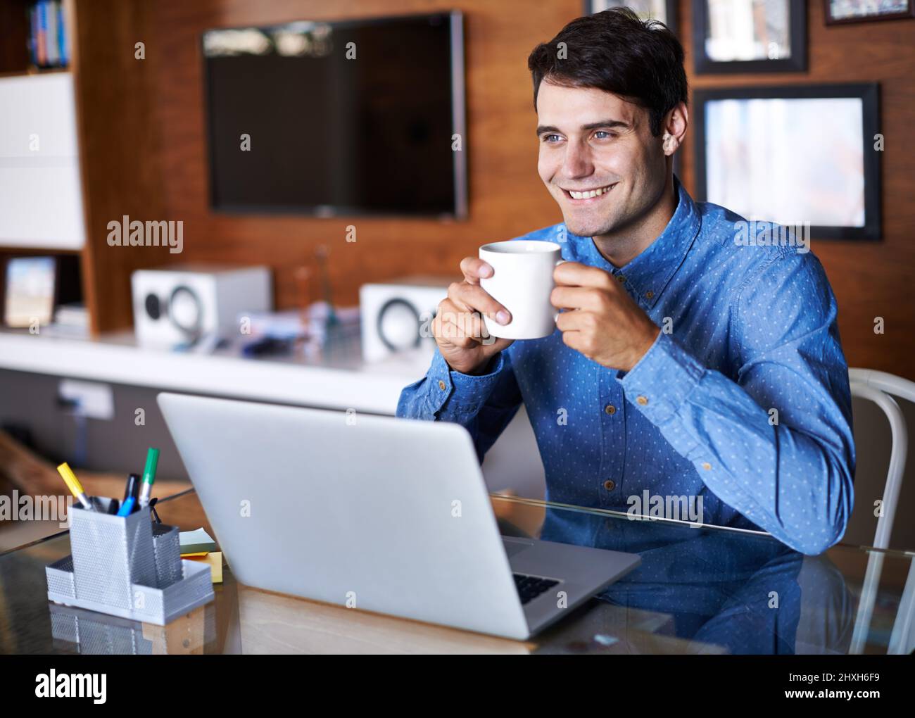 Seinen Arbeitstag gleich am Morgen zu planen. Ein junger Geschäftsmann trinkt Kaffee, während er mit einem Laptop an seinem Schreibtisch sitzt. Stockfoto