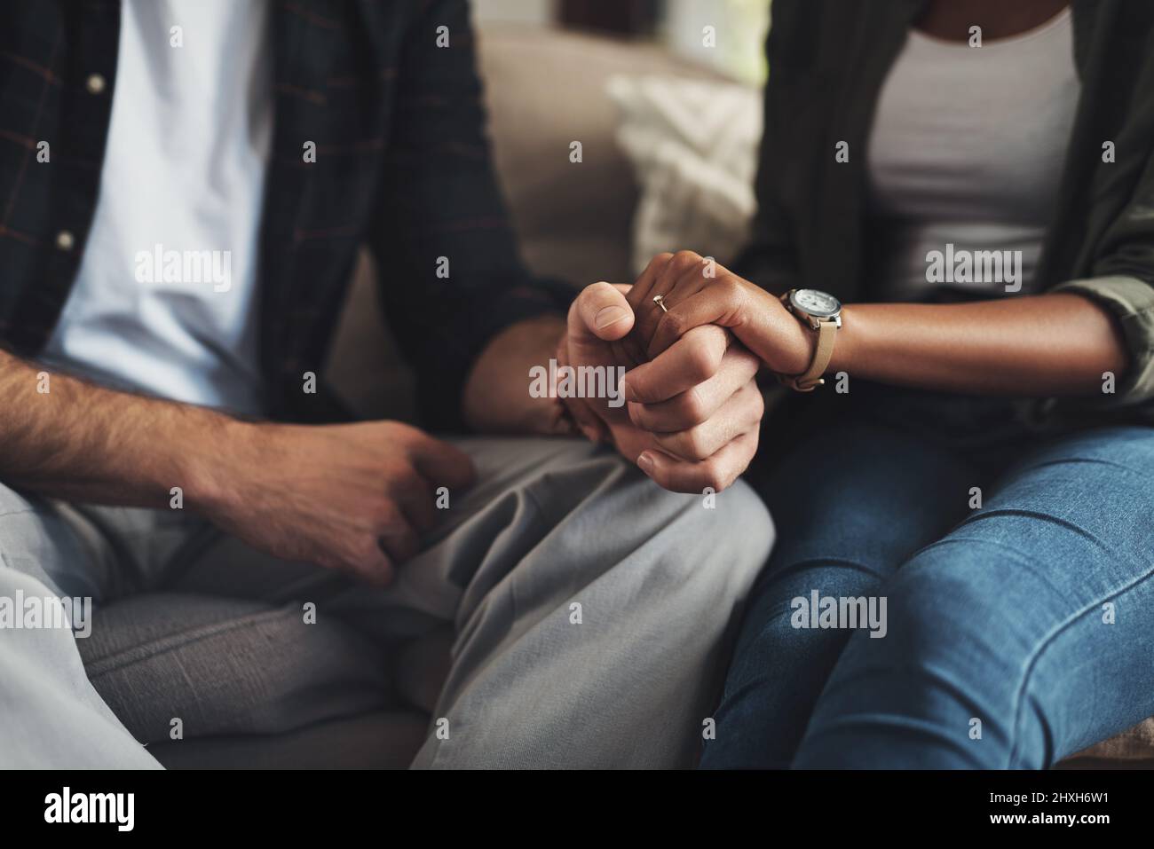 Hand in Hand durch alles. Aufnahme eines unverkennbaren Paares, das die Hände hält, während es zu Hause auf einem Sofa sitzt. Stockfoto