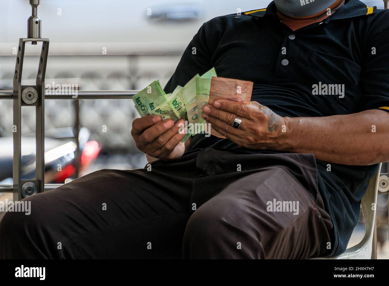 Ein Mann prüft sein Geld. Es sind thailändische Banknoten in einem Hundert-Baht-Schein und zwanzig-Baht-Scheine. Stockfoto