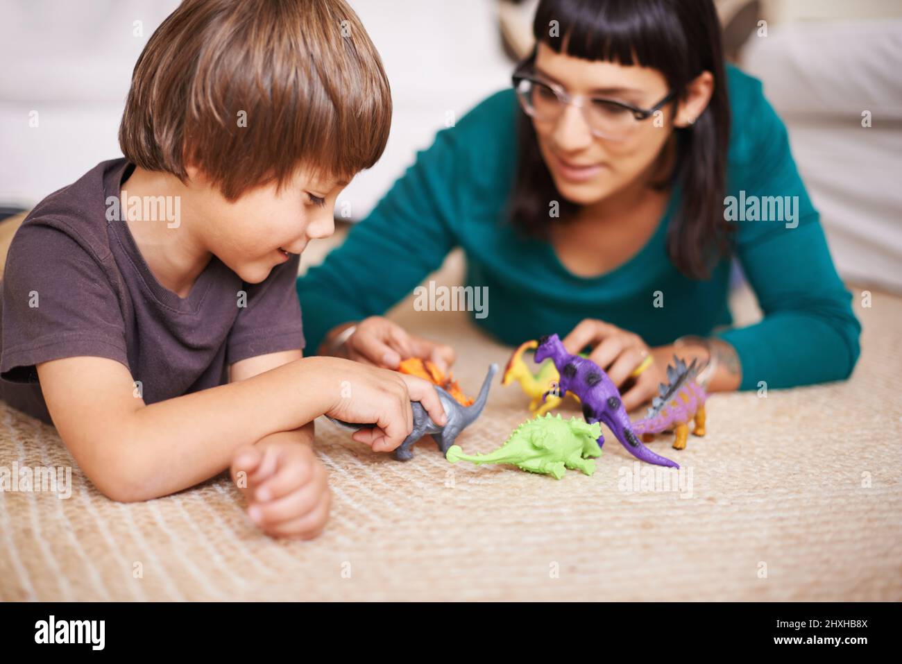 Dinosaurier spielen mit Mama. Ausgeschnittene Aufnahme einer Mutter und ihres Sohnes, die mit Spielzeug-Dinosauriern spielen. Stockfoto