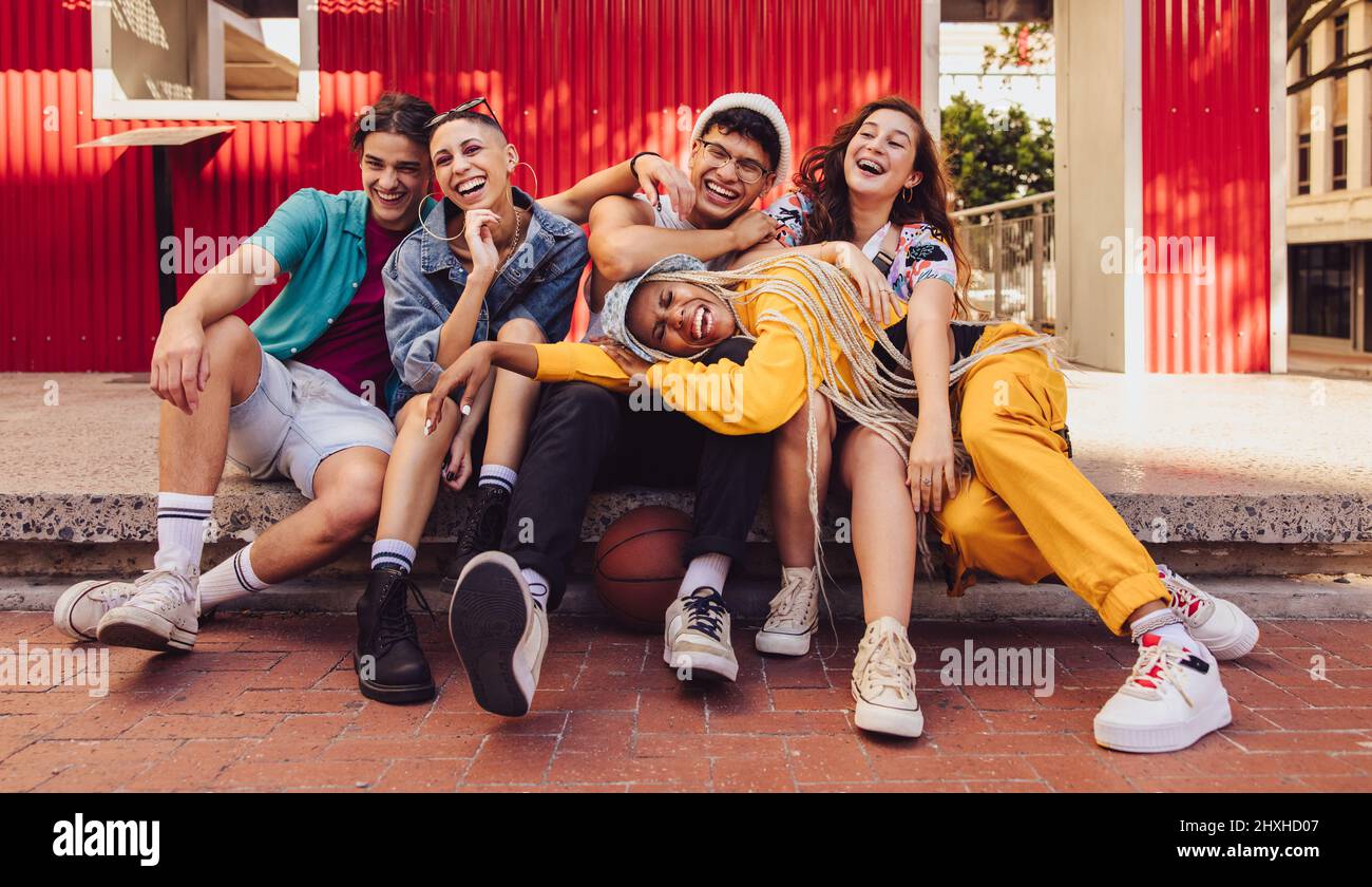 Jugendliche, die gemeinsam Spaß in der Stadt haben. Gruppe von multiethnischen jungen Menschen, die fröhlich lachen, während sie im Freien zusammen sitzen. Lebendige Generation Stockfoto