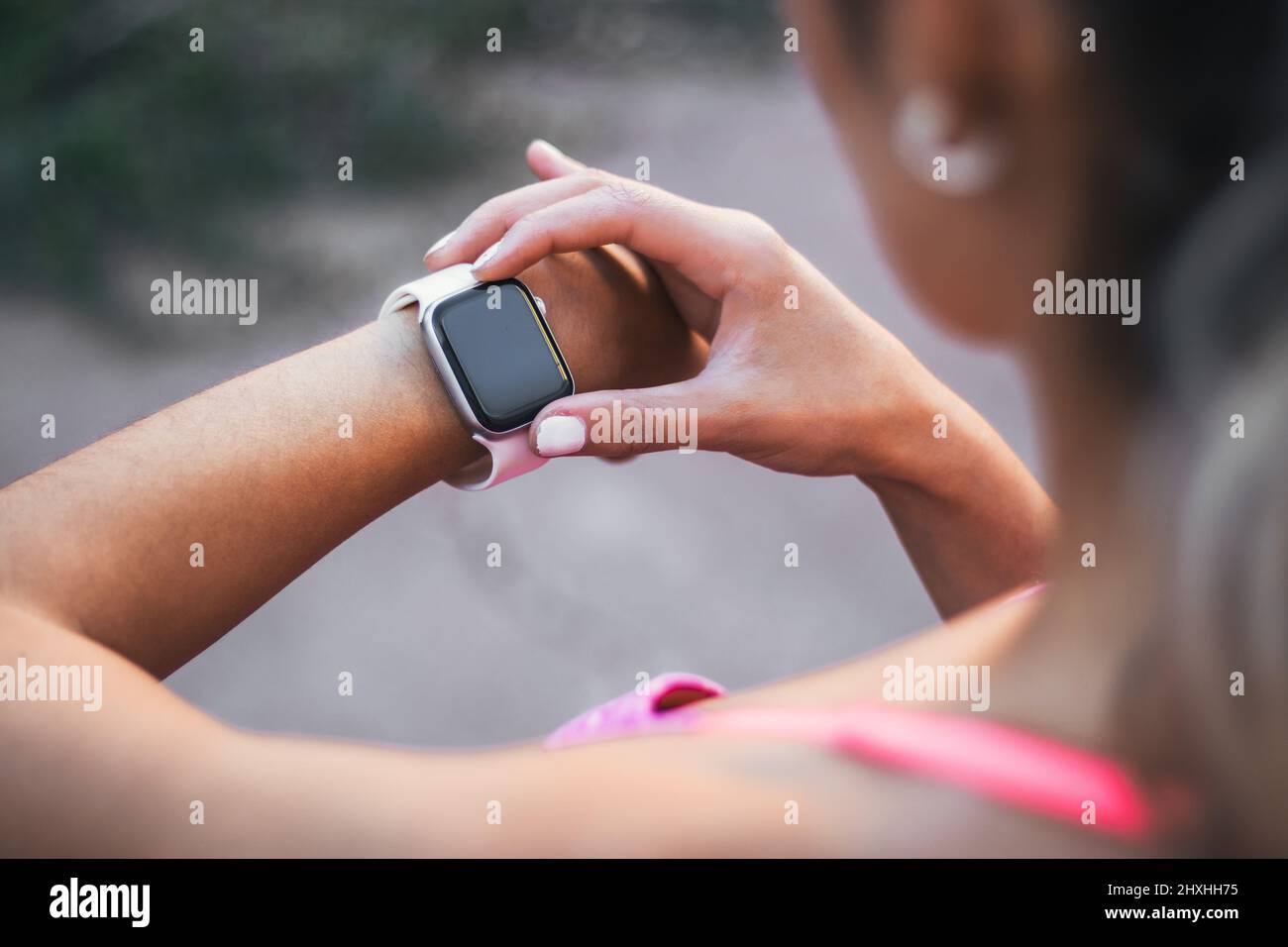 Über die Schulter schauen, wie eine junge aktive Sportlerin ihre Trainingsfortschritte nach dem Laufen mit einer Smart-Watch überwacht Stockfoto