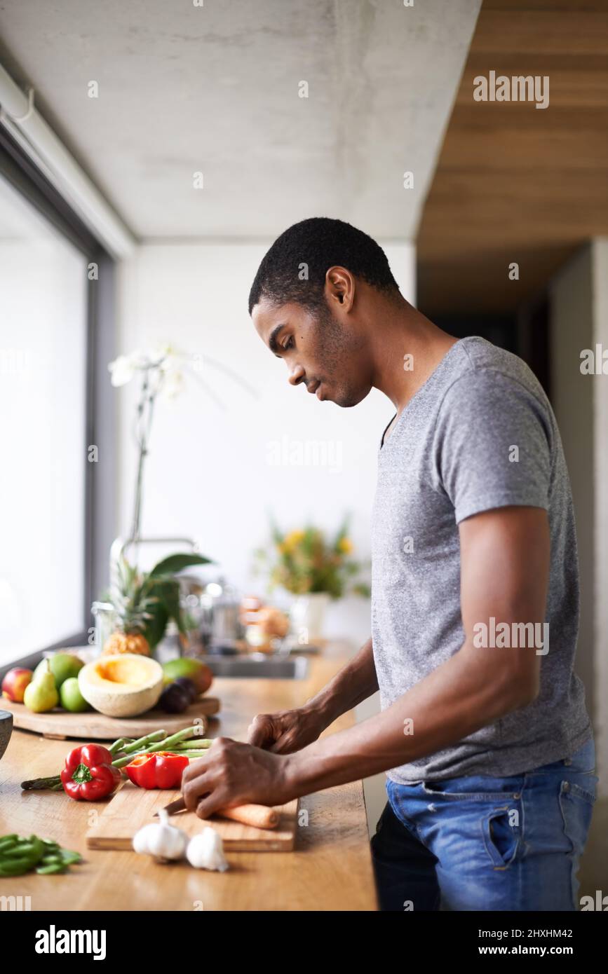 Hes fügt ein wenig Farbe zu seinem Essen hinzu. Aufnahme eines gutaussehenden ethnischen Mannes, der Gemüse im Haus zubereitet. Stockfoto