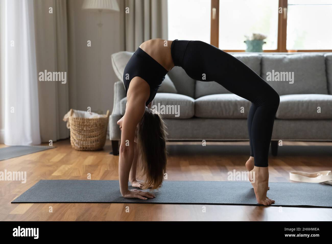 Die Frau trägt schwarze Leggings und ein Oberteil, das zu Hause Asanas übt Stockfoto