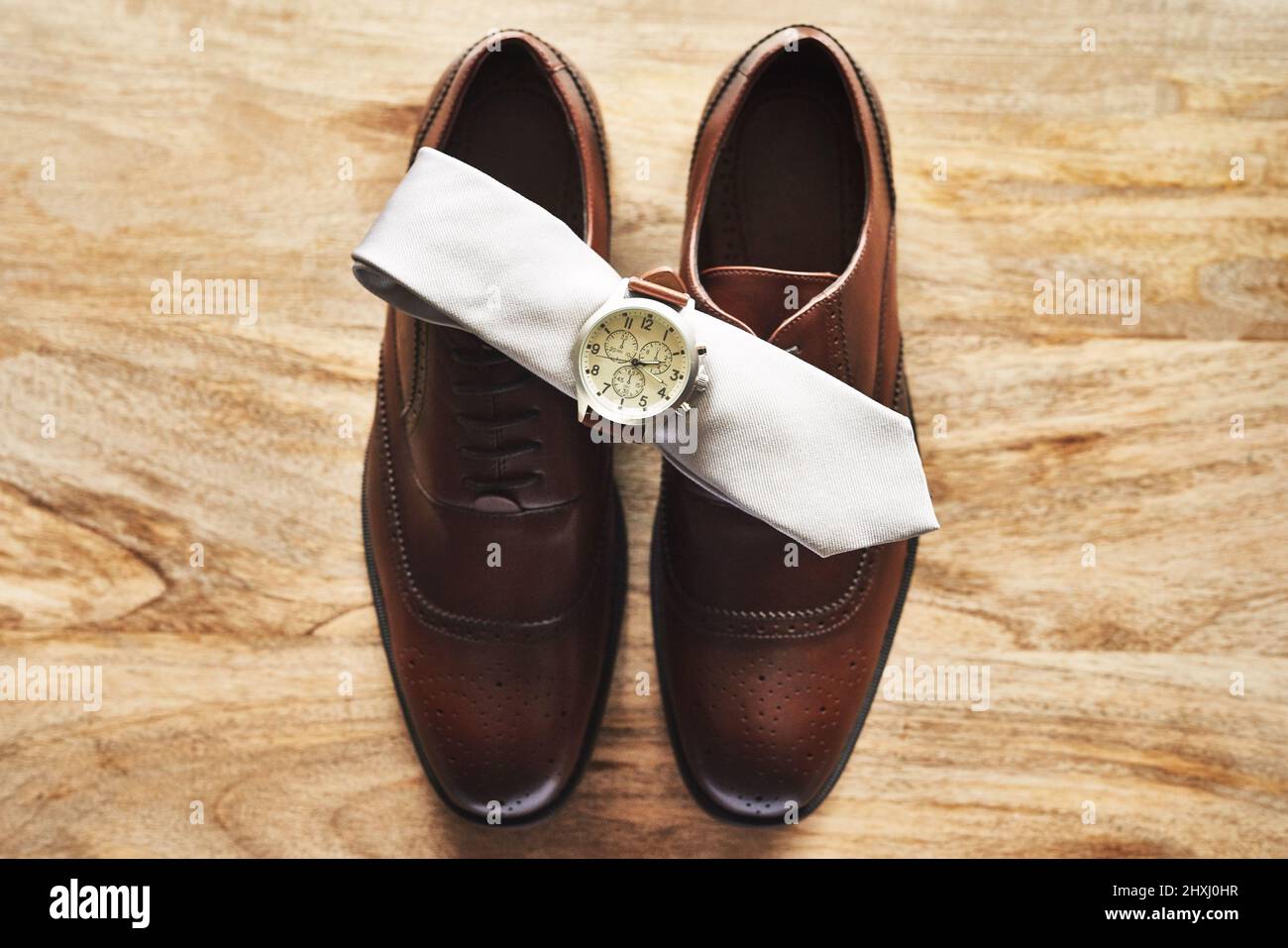 Das dreiteilige Set, das jeder Gentleman haben muss. Stillleben einer Armbanduhr und Krawatte auf formellen Schuhen auf einer Holzoberfläche. Stockfoto