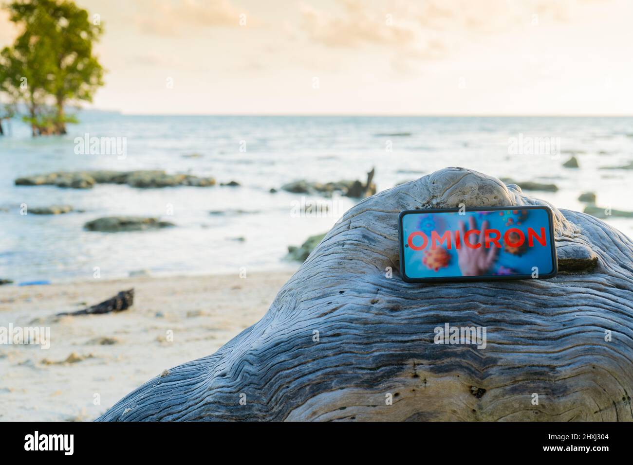 Mobiltelefon auf einem Felsen an einem einsamen Strand platziert, der aufgrund der COVID-Variantenwelle von omicron weltweit Urlaubsreisen und mehr annulliert wurde Stockfoto