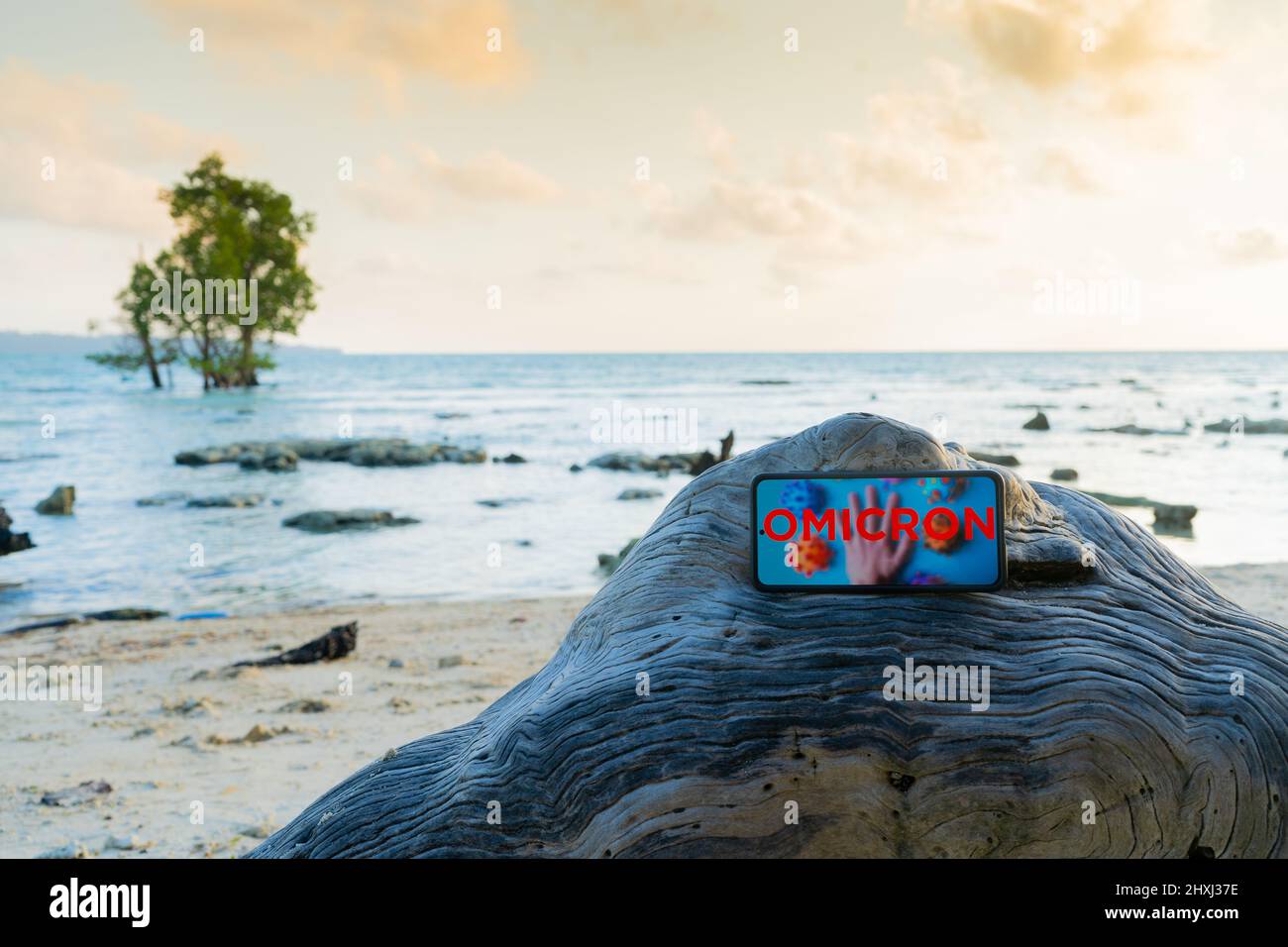 Mobiltelefon auf einem Felsen an einem einsamen Strand platziert, der aufgrund der COVID-Variantenwelle von omicron weltweit Urlaubsreisen und mehr annulliert wurde Stockfoto