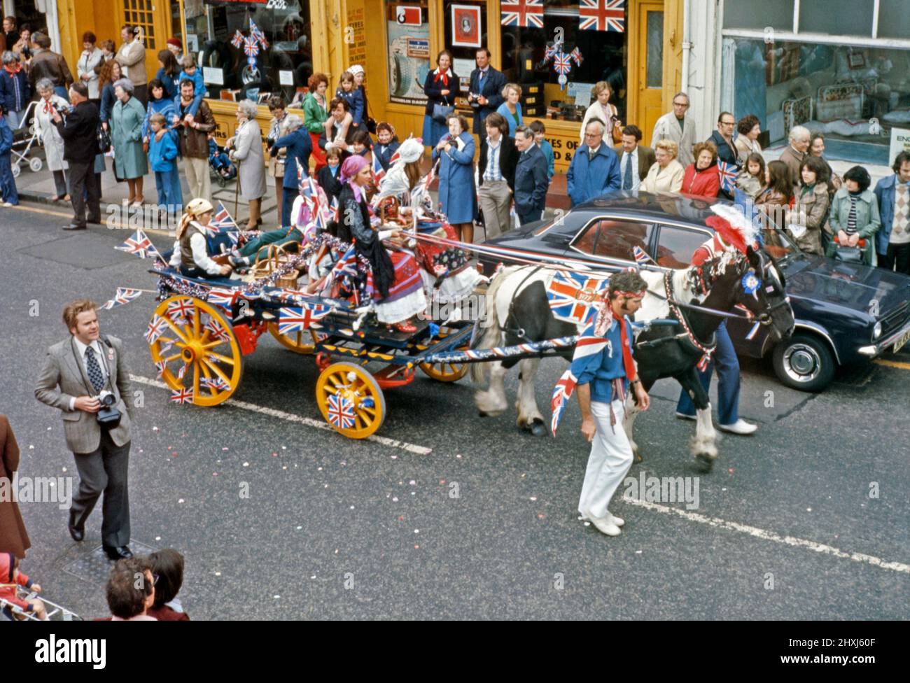 Eine Parade, die am 6. Juni 1977 zur Feier des Silbernen Jubiläums von Königin Elizabeth II. Stattfand Dies fand in Sheen Lane, East Sheen, im Londoner SW14, England, statt. Hier fährt ein Zigeunerpferd und ein Wagen die Straße entlang. Union Jack Flaggen in allen Größen sind zu sehen. Der 25. Jahrestag der Krönung der Königin fand am 6. Februar 1977 statt, aber der 7. Juni war für einen wichtigen offiziellen und inoffiziellen Feiertag im ganzen Land bestimmt. Dieses Bild stammt aus einer alten Amateur-Farbtransparenz – einem Vintage-Foto aus dem Jahr 1970s. Stockfoto