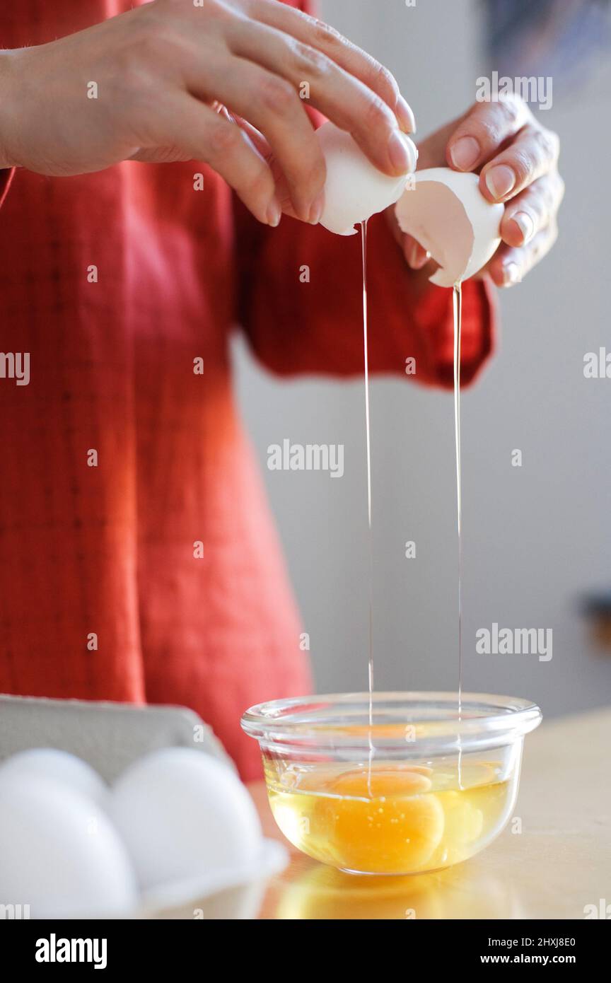 Zubereitung von Speisen, Hände, die ein rohes Ei aufbrechen. Stockfoto