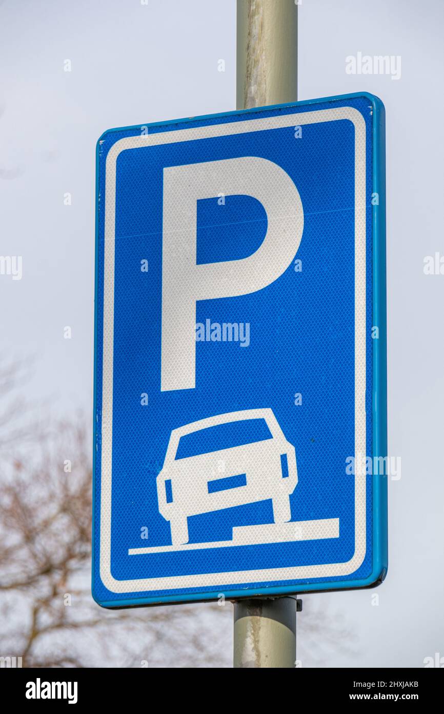 Parkplatzschild auf einem Teil des Bürgersteiges, blaue rechteckige Metall-Vertikalplatte mit einer Zeichnung eines Autos auf dem Bürgersteig in weißem, unscharfem Hintergrund, Stockfoto