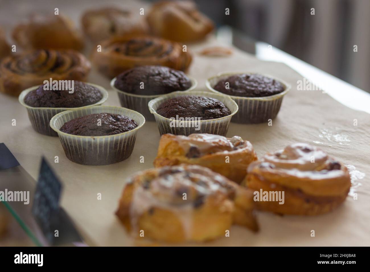 Verschiedene gebackene Muffins und Brötchen in Glasvitrine im Bäckercafe. Donuts und Ringe. Im Café liegen heiße Backwaren auf dem Regal. Brötchen und Schokoladenmuffi Stockfoto