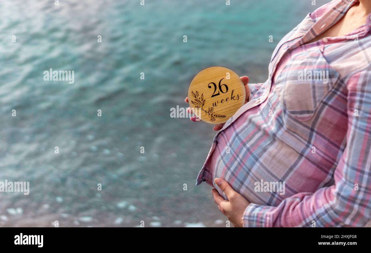 26 Wochen schwanger Frau mit einer Schwangerschaftskarte am Meer. Schwangerschaft Foto-Shooting-Konzept. Schwangerschaft und Mutterschaft. Fotoshooting mit Meerblick Stockfoto