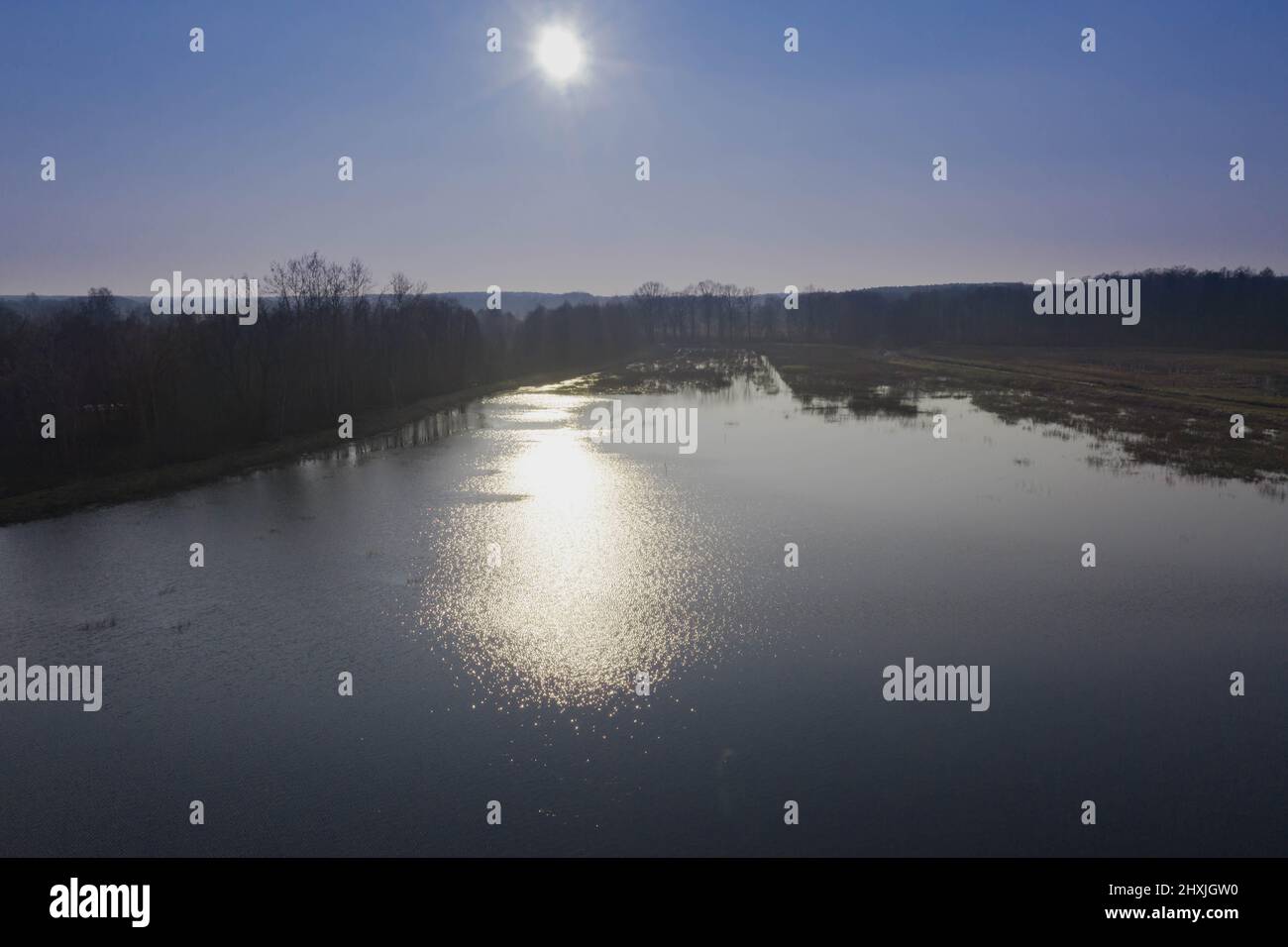 Ein See, ein Wasserreservoir inmitten von Wäldern. Die Ufer sind mit gelben, trockenen Schilf bedeckt. Das Sonnenlicht wird im Wasser reflektiert. Stockfoto