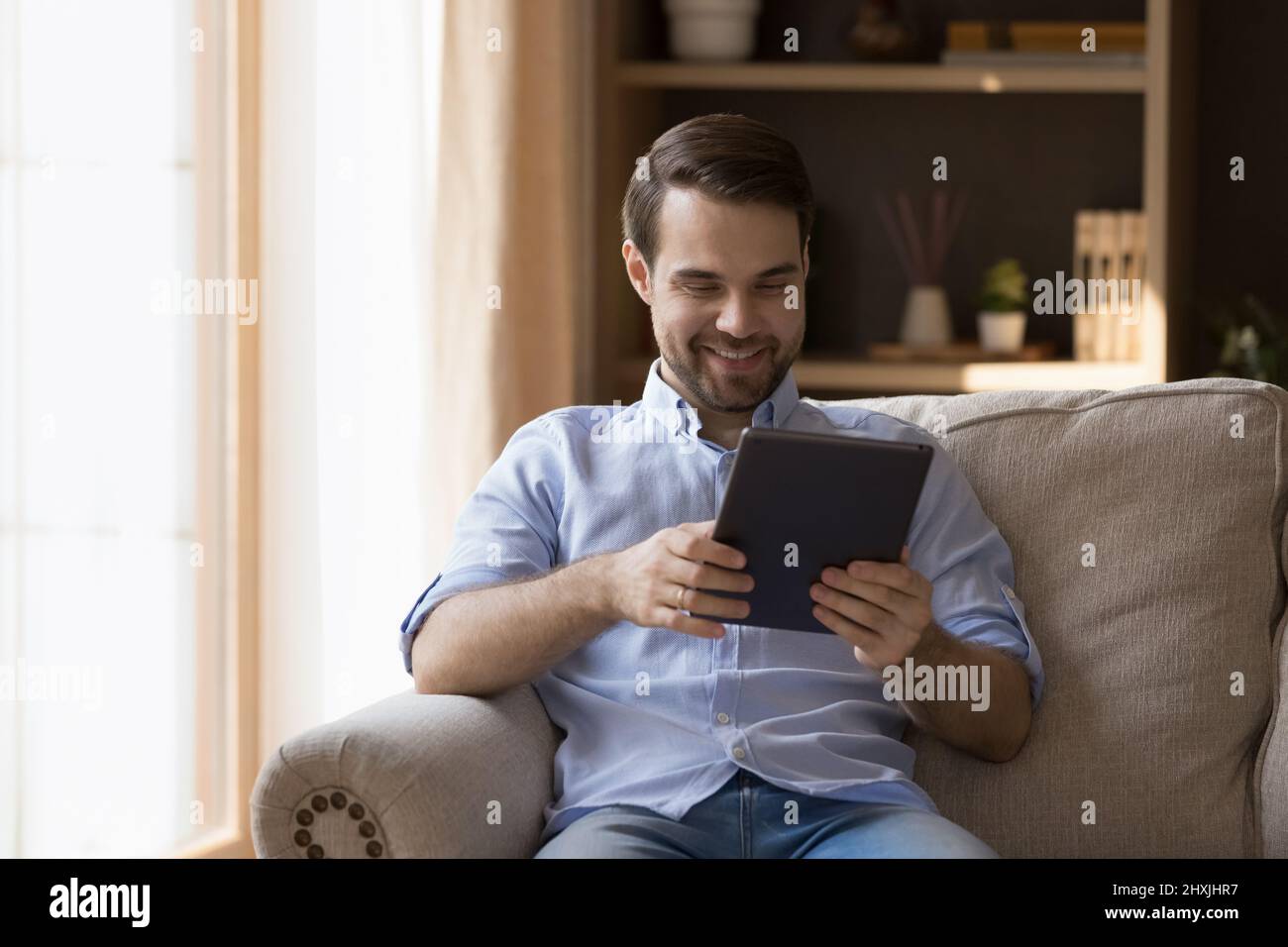 Fröhlicher Tausendjähriger Mann ruht sich auf der Couch aus und schaut euch das Video auf dem Touchpad an Stockfoto