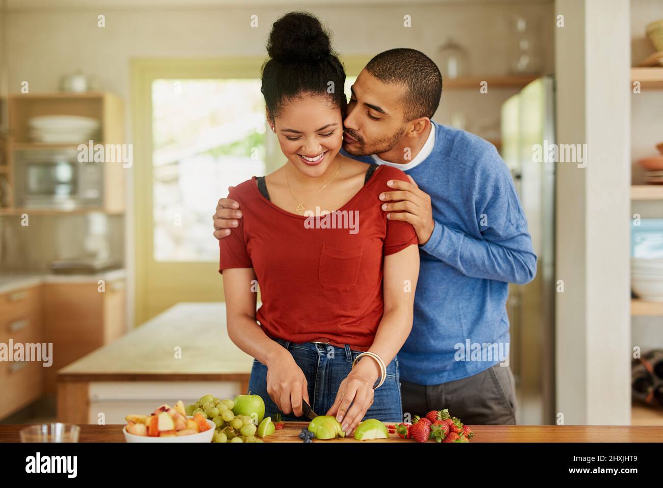 Sich gegenseitig dabei zu unterstützen, die gesündesten zu sein, die sie sein können. Aufnahme eines jungen Mannes, der seine Frau küsst, während sie zu Hause einen gesunden Snack zubereitet. Stockfoto