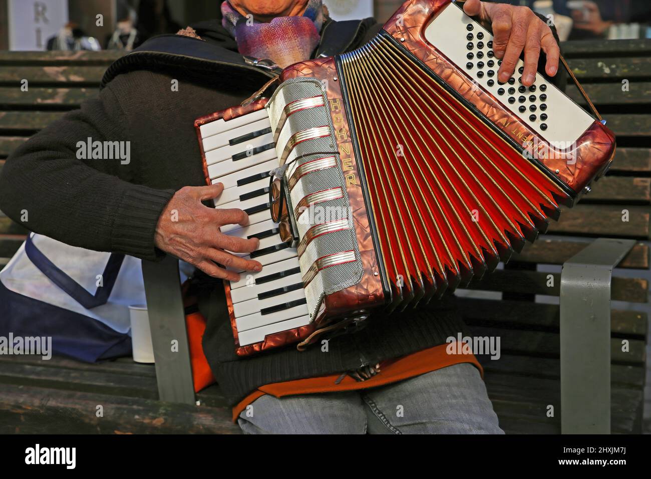 Düsseldorf, Deutschland - März 9. 2022: Nahaufnahme eines nicht erkennbaren alten Mannes, der auf einer Bank sitzt und auf einer öffentlichen Straße zweihändige hohner Student Piano Akkordeon spielt Stockfoto