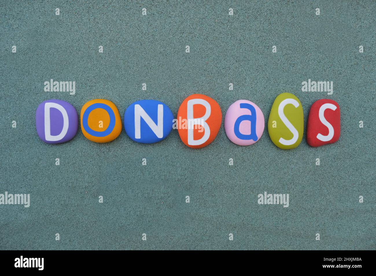 Donbass, historische, kulturelle und wirtschaftliche Region im Südosten der Ukraine, komponiert mit handbemalten mehrfarbigen Steinbuchstaben über grünem Sand Stockfoto