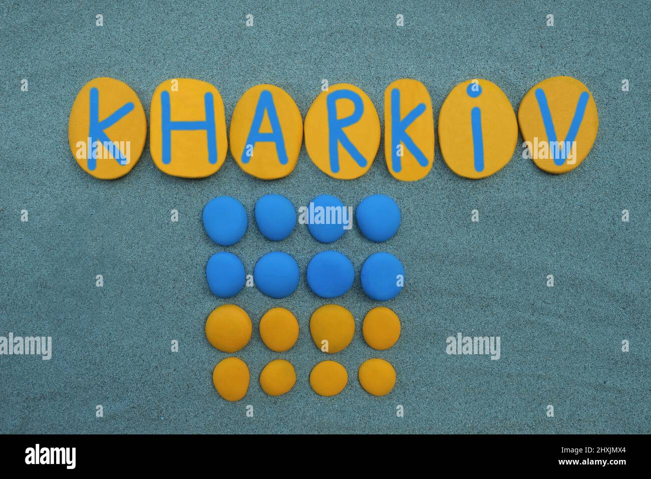 Kharkiv, Ukraine, kreativer Text, komponiert mit blauen und gelben handbemalten Steinen über grünem Sand Stockfoto