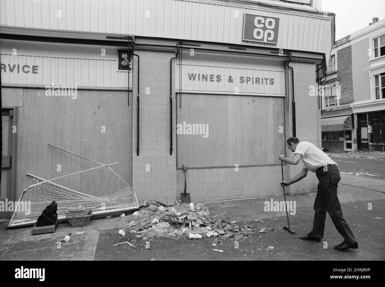 Die Säuberung begann in den Straßen von Notting Hill nach den Unruhen am montagabend nach dem Karneval. Ein Co-Op-Mitarbeiter beginnt die große Aufgabe, den Trümmer zu fegen. 31.. August 1976. Stockfoto