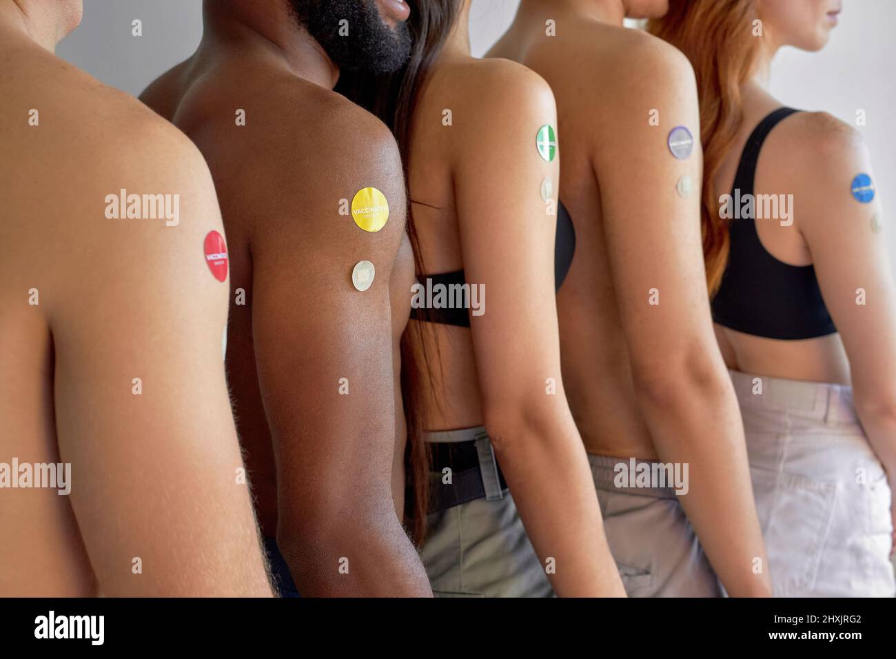 Junge Menschen stehen in der Schlange, nach der Impfung in der Schlange. Drinnen. Seitenansicht, Nahaufnahme der Arme. Kurzgeschnittene, nicht erkennbare Männer und Frauen mit unterschiedlicher Haut Stockfoto