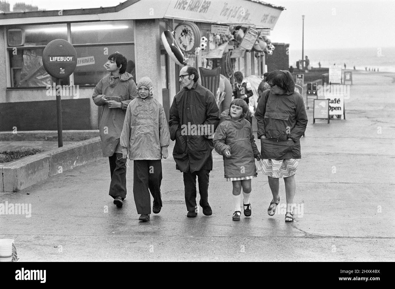 East Riding of Yorkshire, eine Familie, die trotz der Wetterbedingungen das Beste aus einem Spaziergang am Hornsea Sea Front macht. 8.. August 1977 Stockfoto