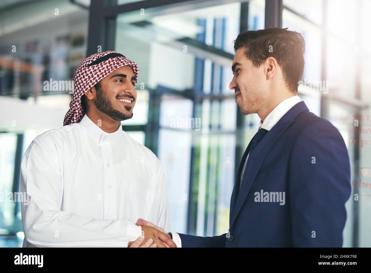 Unternehmen, die auf einem gemeinsamen Ziel aufbauen. Aufnahme eines jungen muslimischen Geschäftsmannes, der in einem modernen Büro mit einem Mitarbeiter die Hände schüttelt. Stockfoto