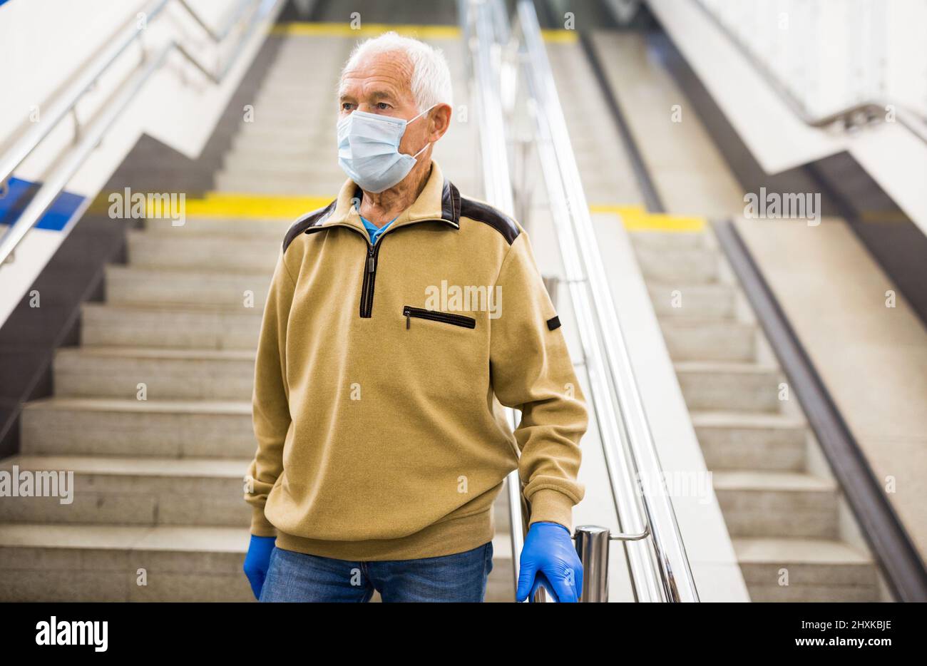 Ein älterer Mann mit Schutzmaske und Handschuhen steigt die Treppe zur U-Bahn-Station hinunter. Konzept des Schutzes während der COVID-Pandemie Stockfoto