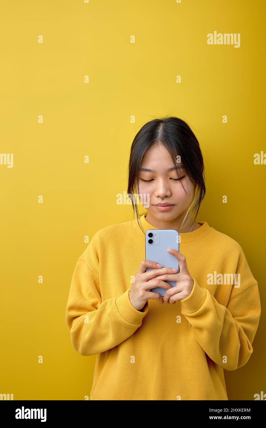 Asiatische schöne Frau in gelbem Hemd stehend halten Handy in den Händen, bereiten Sie einen Anruf zu machen. Menschen- und Technologiekonzept.Chinesische Dame chatt Stockfoto