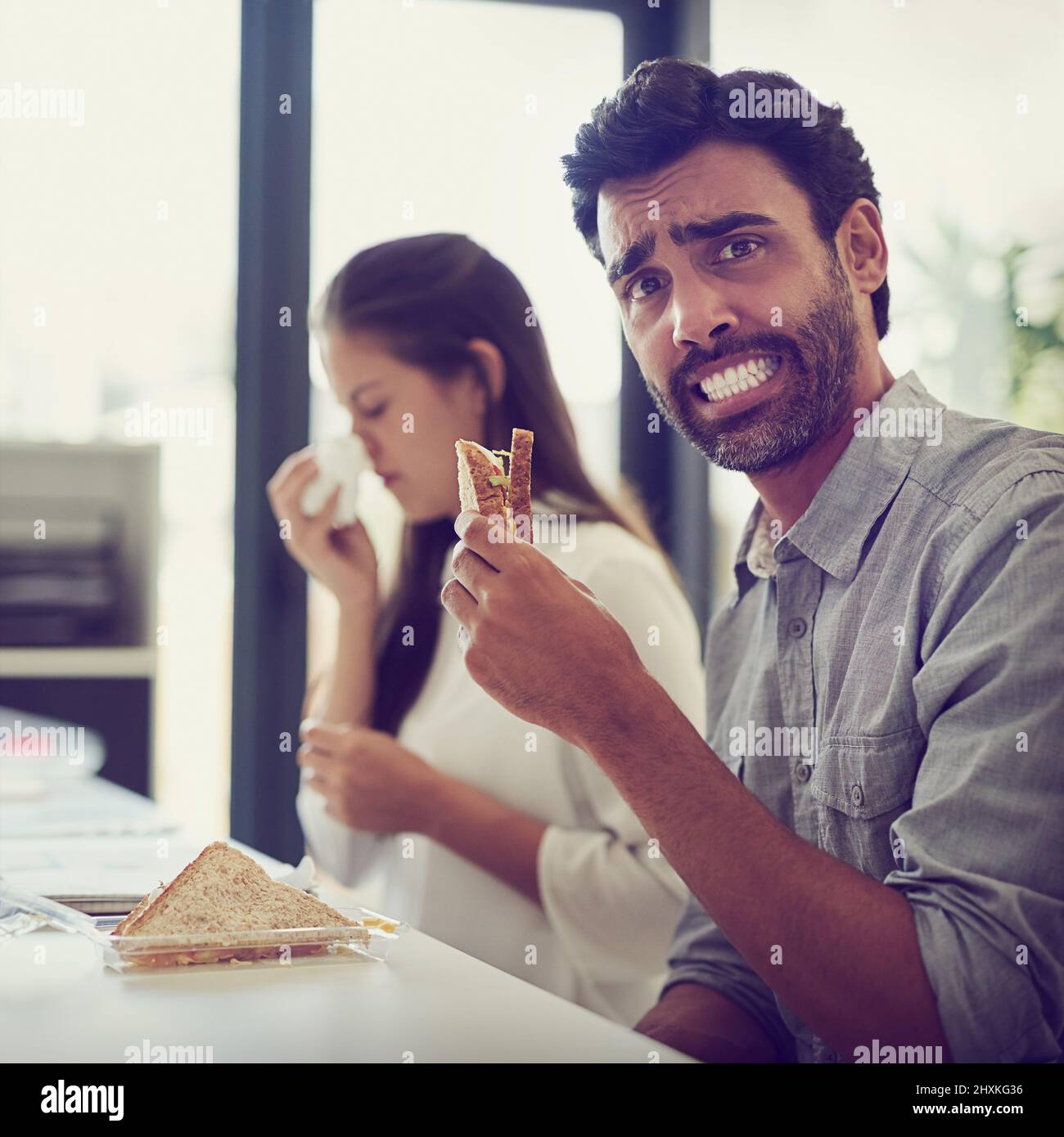 Ich hoffe, ich fange ihre Keime nicht ein. Porträt eines Geschäftsmannes, der angewidert aussieht, während er neben einem Kollegen sitzt, der an Allergien leidet. Stockfoto