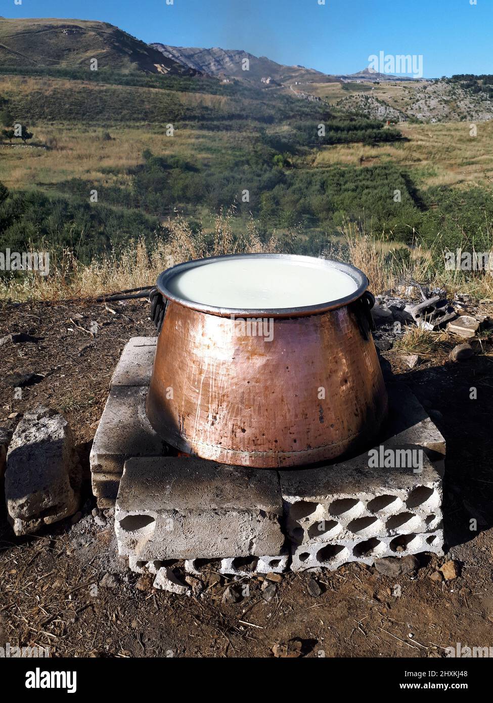 Frische Milch in einem großen Messingbehälter, der als erster Schritt zur Käseherstellung gekocht wird. Stockfoto