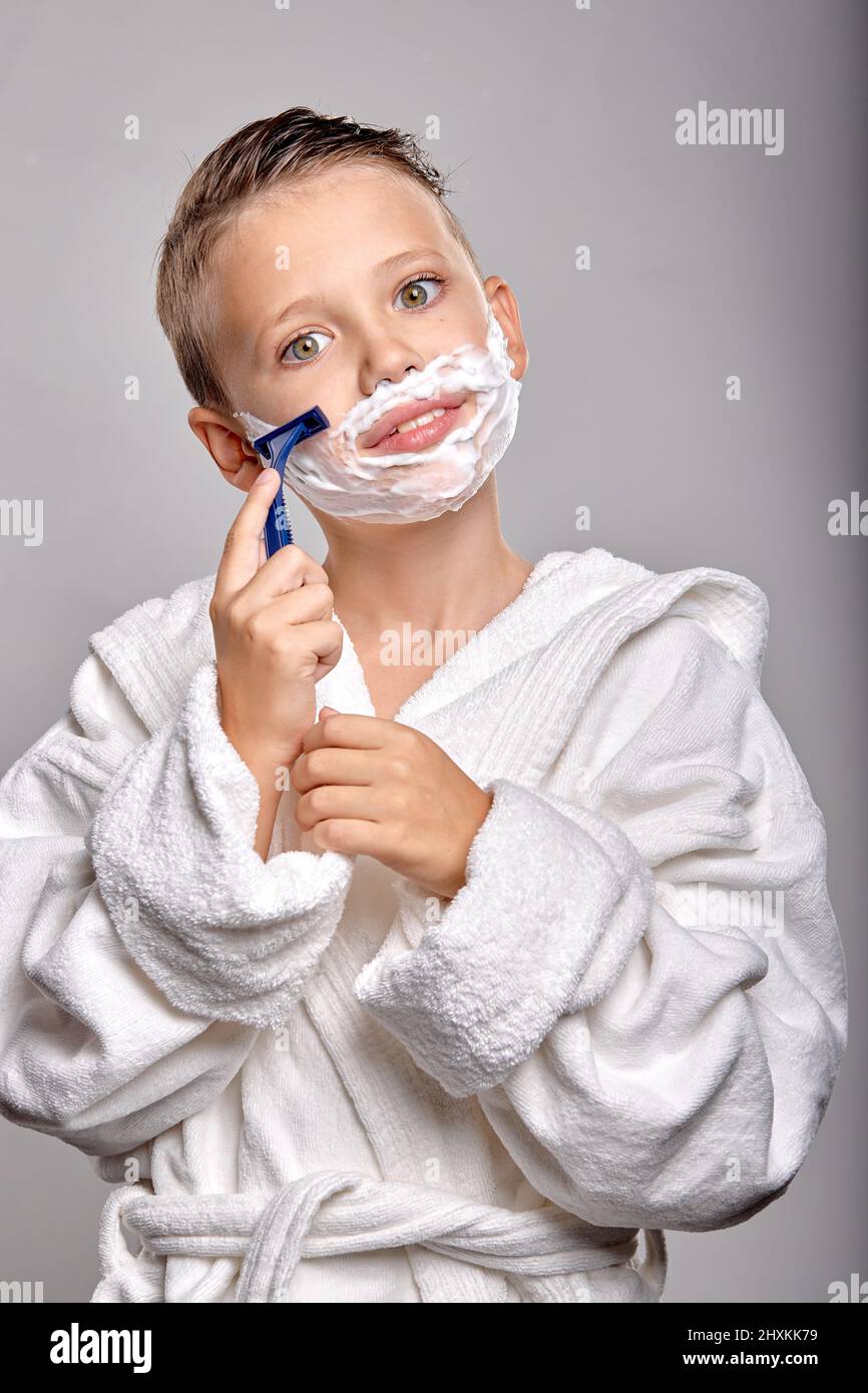 Glückliches Kind Junge Sohn mit angenehmen Aussehen, haben Rasierschaum auf  Gesicht, halten Rasiermesser und gehen zu rasieren, stehen in Schaum des  Spiegels isoliert auf grauem Rücken Stockfotografie - Alamy
