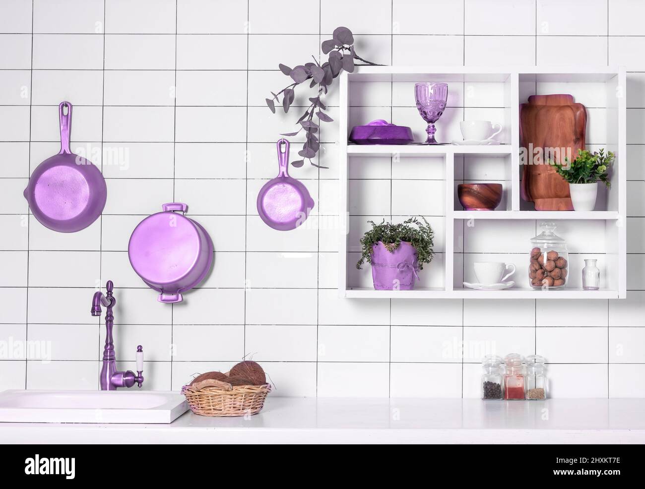 Moderne Küchenausstattung mit weißen Fliesen, Regalen, Pflanzen und violettem Küchengeschirr an der Wand. Hochwertige Fotos Stockfoto