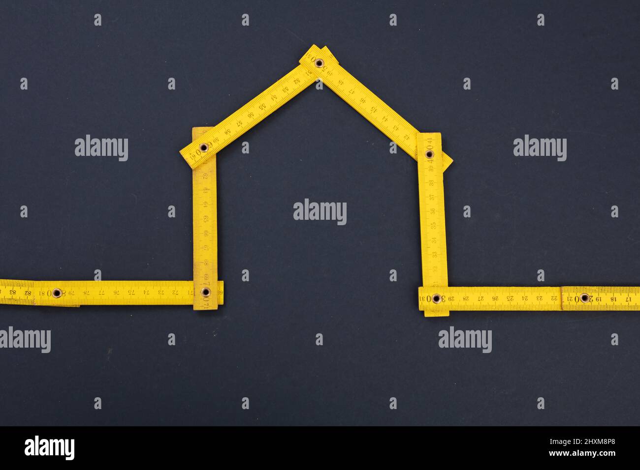 Hausreparatur. Hausform gelb Holzmaß, grau schwarzer Hintergrund. Falzlineal, Werkstatt, diy, Handwerker-Konzept. Stockfoto