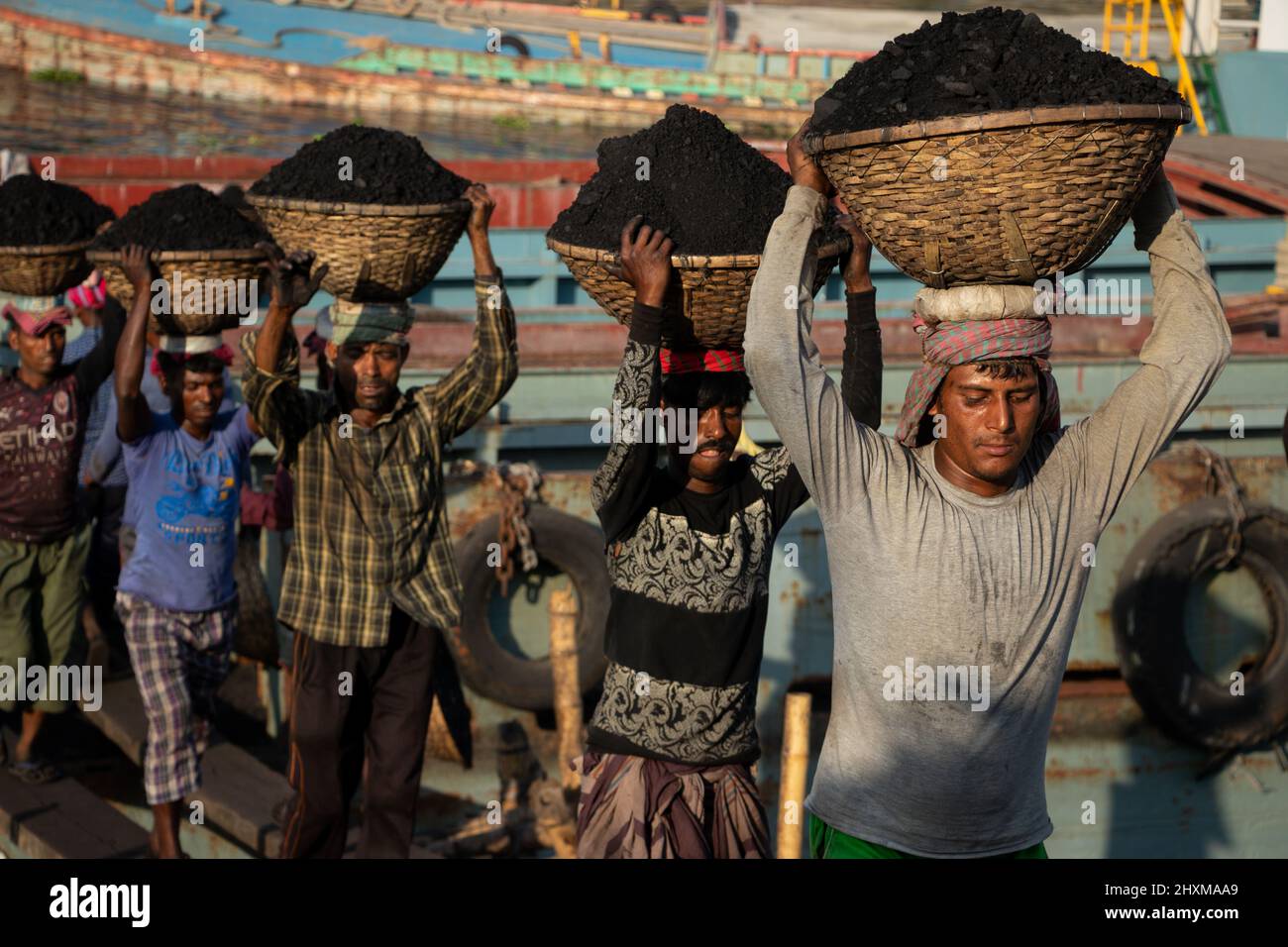 Dhaka, Dhaka, Bangladesch. 13. März 2022. Arbeiter transportieren Körbe voller Kohle auf ihren Köpfen, während sie Kohle von einem Frachtschiff in Dhaka, Bangladesch, entladen. Etwa 3,0 Prozent der Energie des Landes stammt derzeit aus Kohle. An diesen Häfen werden kohlebeladene Güter aus Indien, Indonesien und Afrika verladen. Tagelöhner verdienen rund $1 für je 30 Körbe Kohle, die vom Schiff entladen werden. Am frühen Morgen beginnen die Arbeiter, Kohlen bis zum Sonnenuntergang zu entladen, sie verdienen $5 bis $7 Dollar pro Tag. Es gibt keine speziellen Schuhe an ihren Füßen und keine Handschuhe in ihren Händen, um Kohle von Frachtschiffen zu entladen. Moreo Stockfoto