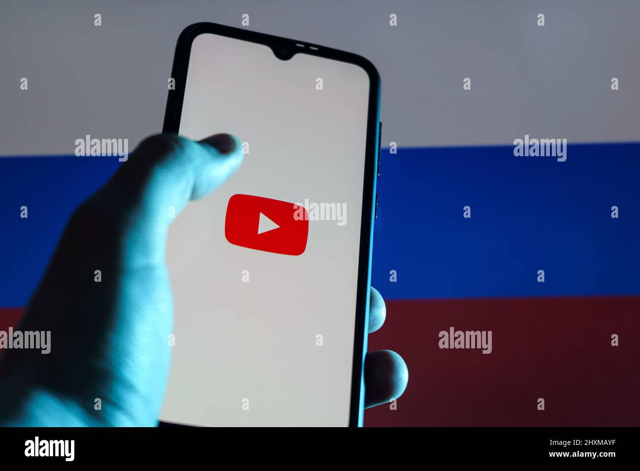YouTube-Anwendung auf dem Smartphone. Russische Flagge im Hintergrund. YouTube-Verbot in Russland Stockfoto