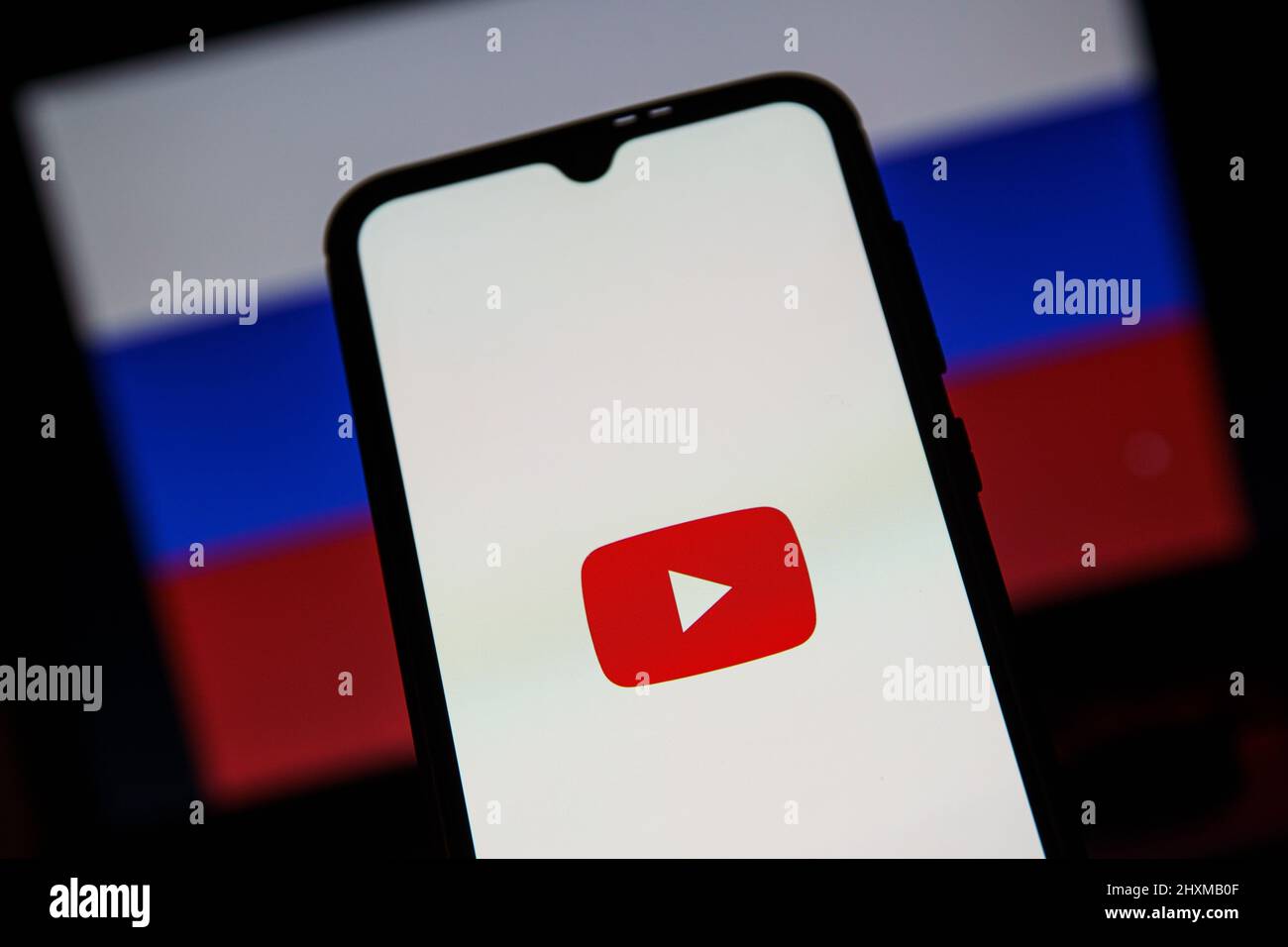 YouTube-Anwendung auf dem Smartphone. Russische Flagge im Hintergrund. YouTube-Verbot in Russland Stockfoto