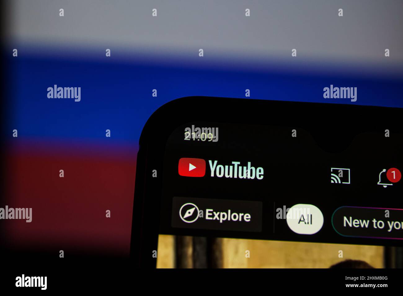 YouTube-Anwendung auf dem Smartphone. Russische Flagge im Hintergrund. YouTube-Verbot in Russland Stockfoto