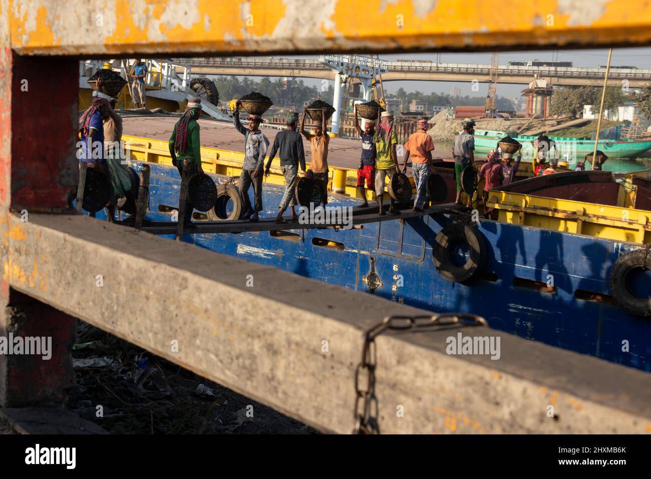 Dhaka, Dhaka, Bangladesch. 13. März 2022. Arbeiter transportieren Körbe voller Kohle auf ihren Köpfen, während sie Kohle von einem Frachtschiff in Dhaka, Bangladesch, entladen. Etwa 3,0 Prozent der Energie des Landes stammt derzeit aus Kohle. An diesen Häfen werden kohlebeladene Güter aus Indien, Indonesien und Afrika verladen. Tagelöhner verdienen rund $1 für je 30 Körbe Kohle, die vom Schiff entladen werden. Am frühen Morgen beginnen die Arbeiter, Kohlen bis zum Sonnenuntergang zu entladen, sie verdienen $5 bis $7 Dollar pro Tag. Es gibt keine speziellen Schuhe an ihren Füßen und keine Handschuhe in ihren Händen, um Kohle von Frachtschiffen zu entladen. Moreo Stockfoto