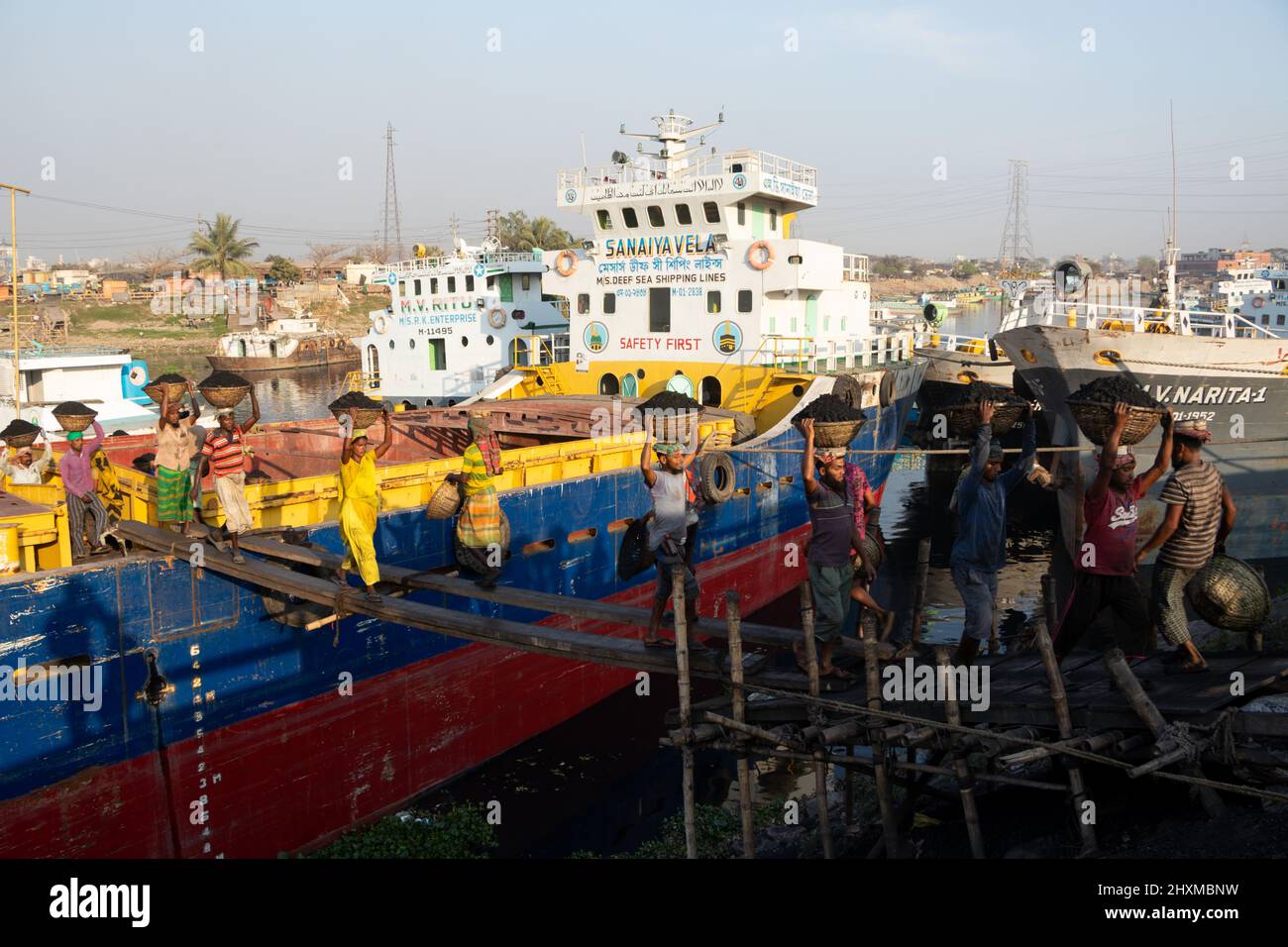 Dhaka, Dhaka, Bangladesch. 13. März 2022. Arbeiter transportieren Körbe voller Kohle auf ihren Köpfen, während sie Kohle von einem Frachtschiff in Dhaka, Bangladesch, entladen. Etwa 3,0 Prozent der Energie des Landes stammt derzeit aus Kohle. An diesen Häfen werden kohlebeladene Güter aus Indien, Indonesien und Afrika verladen. Tagelöhner verdienen rund $1 für je 30 Körbe Kohle, die vom Schiff entladen werden. Am frühen Morgen beginnen die Arbeiter, Kohlen bis zum Sonnenuntergang zu entladen, sie verdienen $5 bis $7 Dollar pro Tag. Es gibt keine speziellen Schuhe an ihren Füßen und keine Handschuhe in ihren Händen, um Kohle von Frachtschiffen zu entladen. Moreo Stockfoto